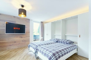 A modern bedroom with a bed, a wall-mounted TV displaying 'NETFLIX', and a wardrobe with sliding doors. - Pool, sauna & ski jump view · #11 (Winterberg)