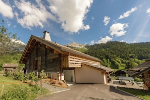 A rustic wooden chalet with a sloped roof, a covered porch, and a view of a mountainous landscape. - New Listing (La Clusaz)