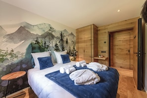 Et hotelværelse med et mural i bjergtema, en seng med sengetøj i hvidt og blå samt møbler af træ.