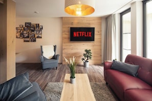 Ein modernes Wohnzimmer mit einem Netflix-Schild, einem blauen Sessel, einem roten Sofa, einem Holztisch und einer Topfpflanze.