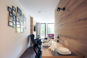 A dining area with a wooden table set for four, a red sofa in the background, and a wall with framed pictures. - Pool & sauna, forest view · #16 (Winterberg)