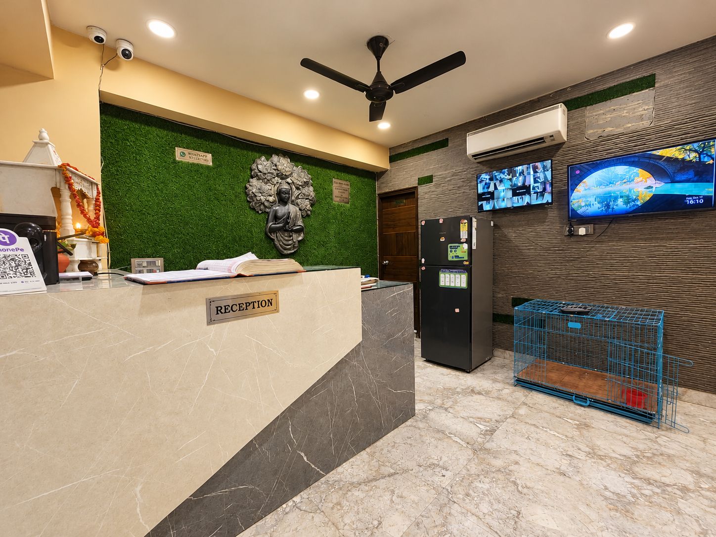 A reception area with a reception desk, a Buddha statue, a refrigerator, a television, and a cage with a red object.