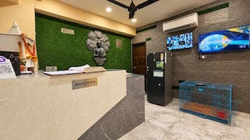 A reception area with a reception desk, a Buddha statue, a refrigerator, a television, and a cage with a red object.