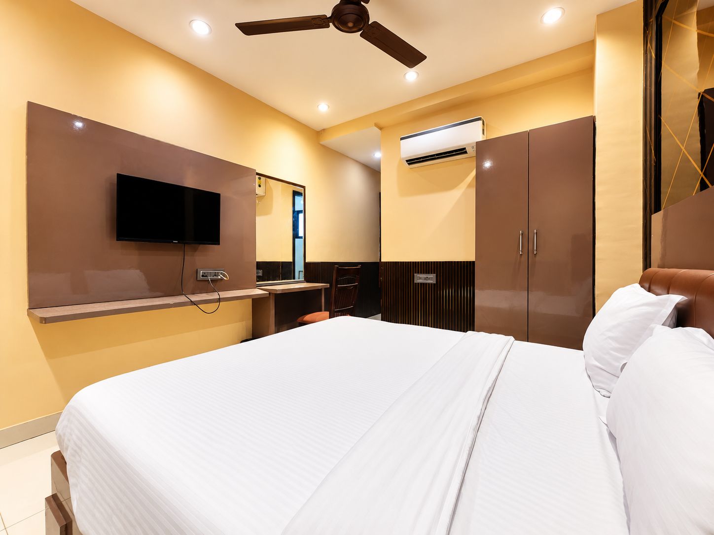 A modern hotel room with a bed, a television, a ceiling fan, and an air conditioning unit.