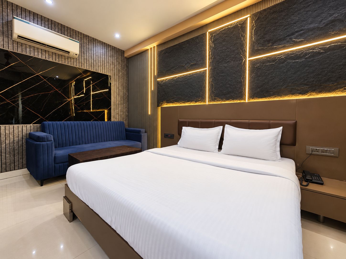 Ett modernt hotellrum med en säng, en blå soffa och en väggmonterad luftkonditioneringsanläggning.