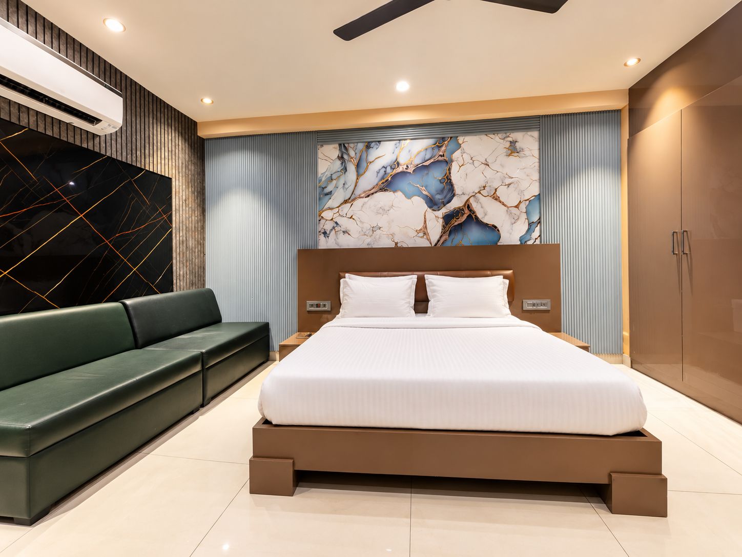 A modern bedroom with a bed, a green sofa, and a marble wall.