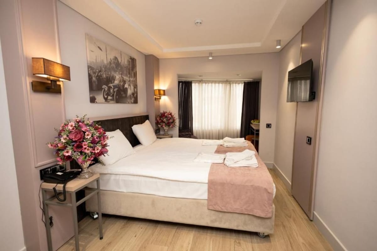 A hotel room with a large bed, bedside lamps, a flat-screen TV, and a painting on the wall.