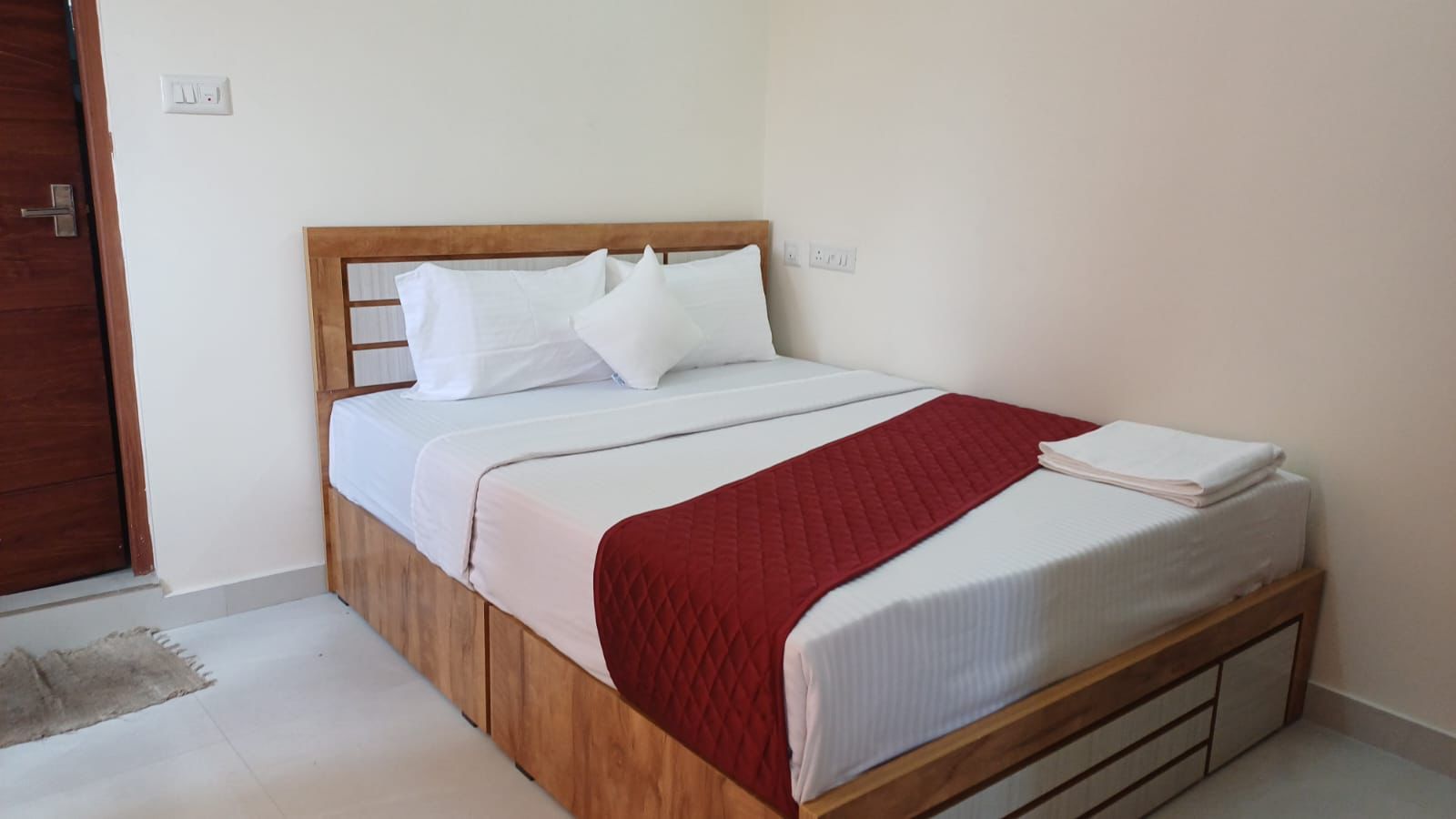 A single bed with a wooden frame, white bedding, and a red blanket.