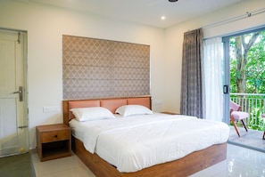 A hotel room with a large bed, a wooden headboard, a nightstand, and a view of greenery through a sliding glass door.