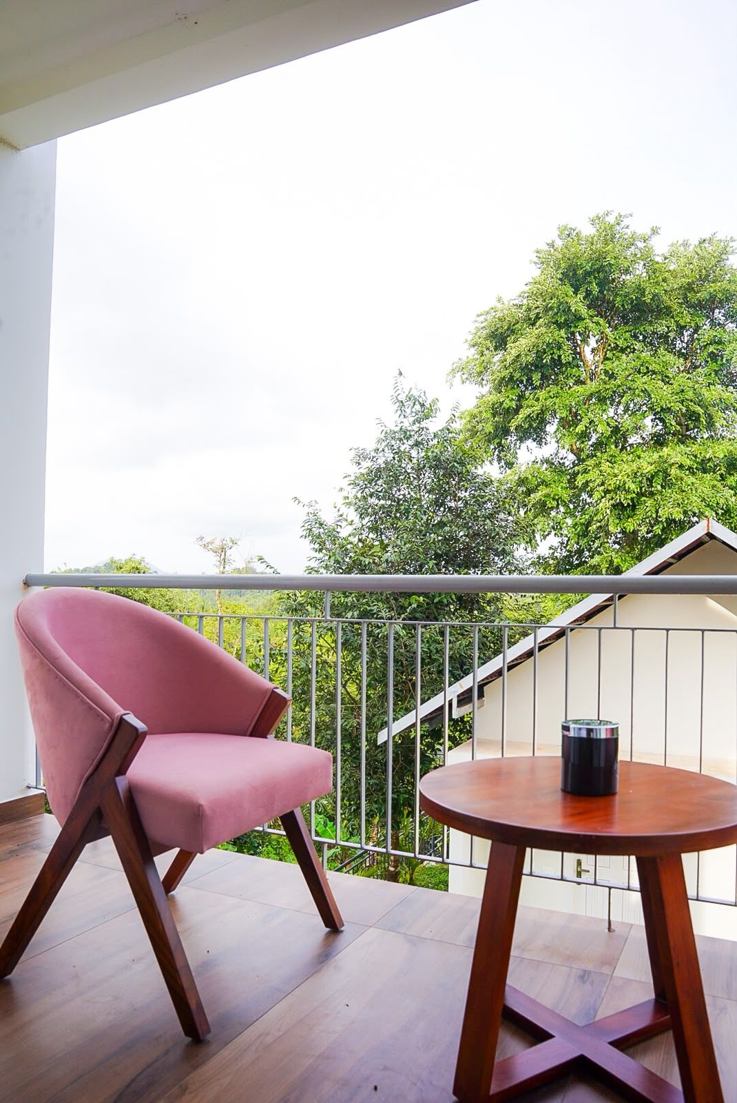 Un balcón con una silla roja y una mesa pequeña, con vistas a un paisaje verde exuberante.