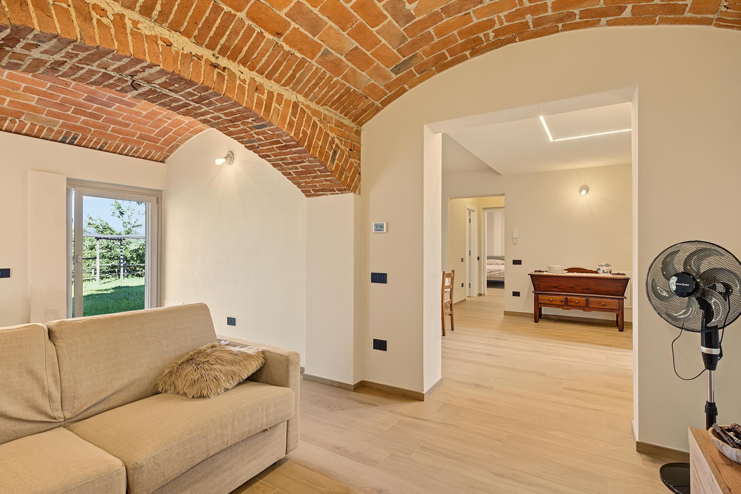 A modern living room with a brick ceiling, a sofa, a dining area with a table and chairs, and a fan.