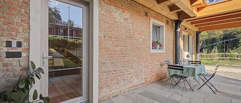 A brick exterior with a glass door entrance, a small table with chairs outside, and a wooden ceiling structure.