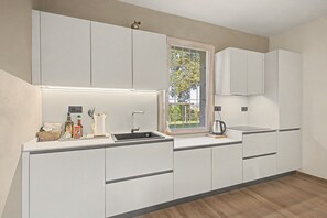 Una cucina moderna con mobili bianchi, un lavello nero e una finestra vista verde.