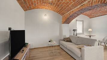 Un soggiorno con soffitto in mattoni, una TV a schermo piatto, un divano, un tavolino con un vaso e una lampada.