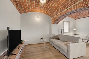 Un salon avec un plafond en briques, un téléviseur à écran plat, un canapé, une petite table sur laquelle est posé un vase, et une lampe.