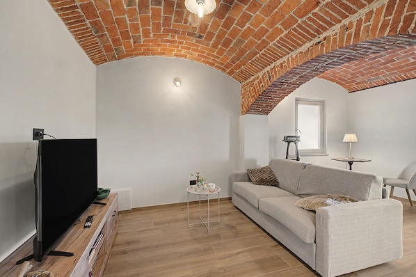 Un soggiorno con soffitto in mattoni, una TV a schermo piatto, un divano, un tavolino con un vaso e una lampada.