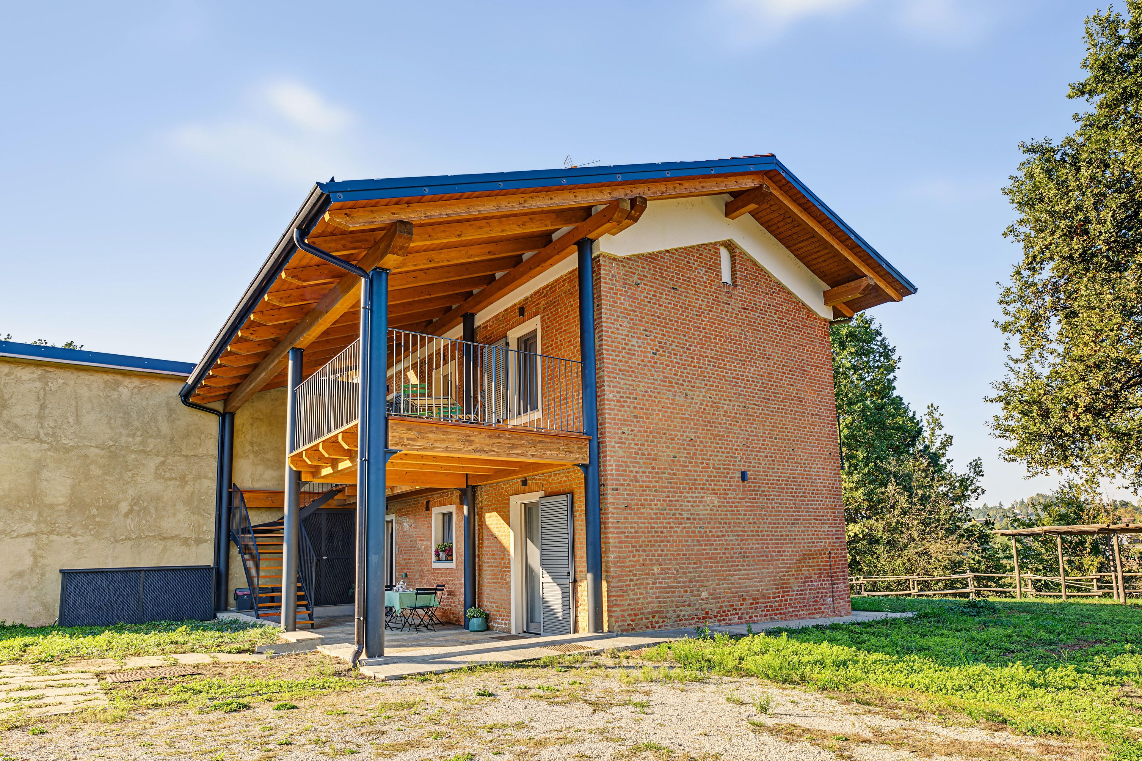Un bâtiment à deux étages avec une façade en briques, un balcon en bois et un espace extérieur abrité avec des sièges.