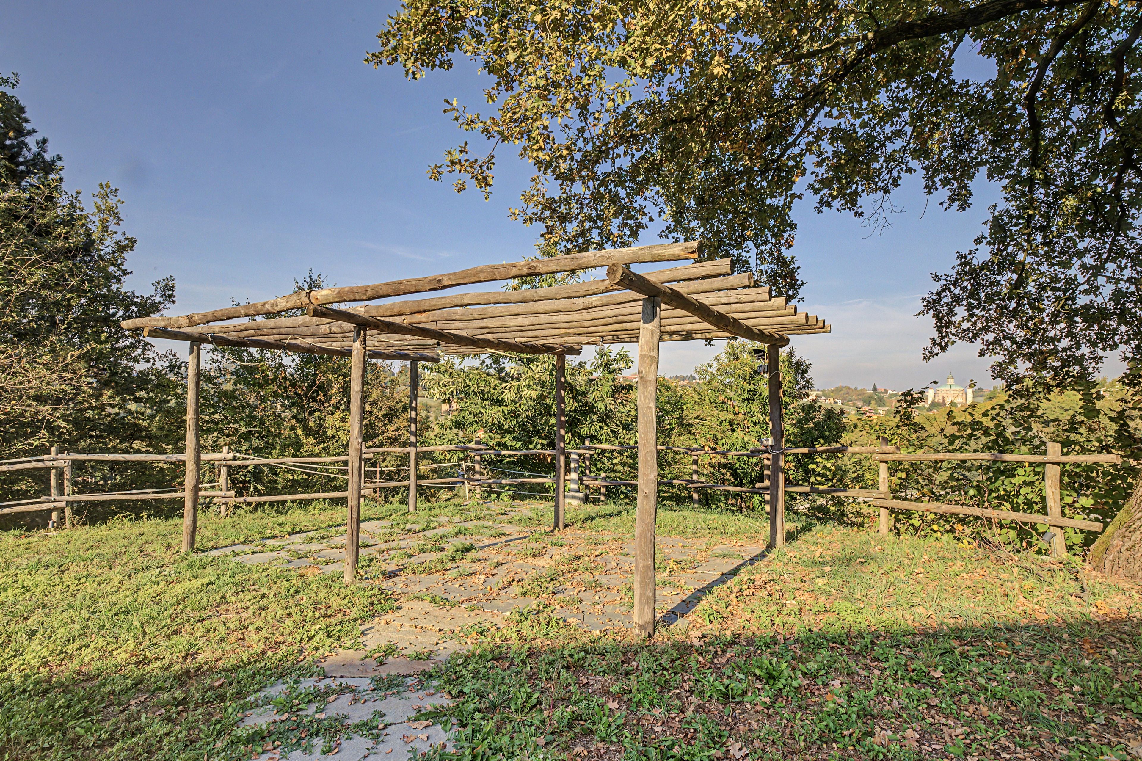 En pergola af træ i en park, omgivet af græs og træer.