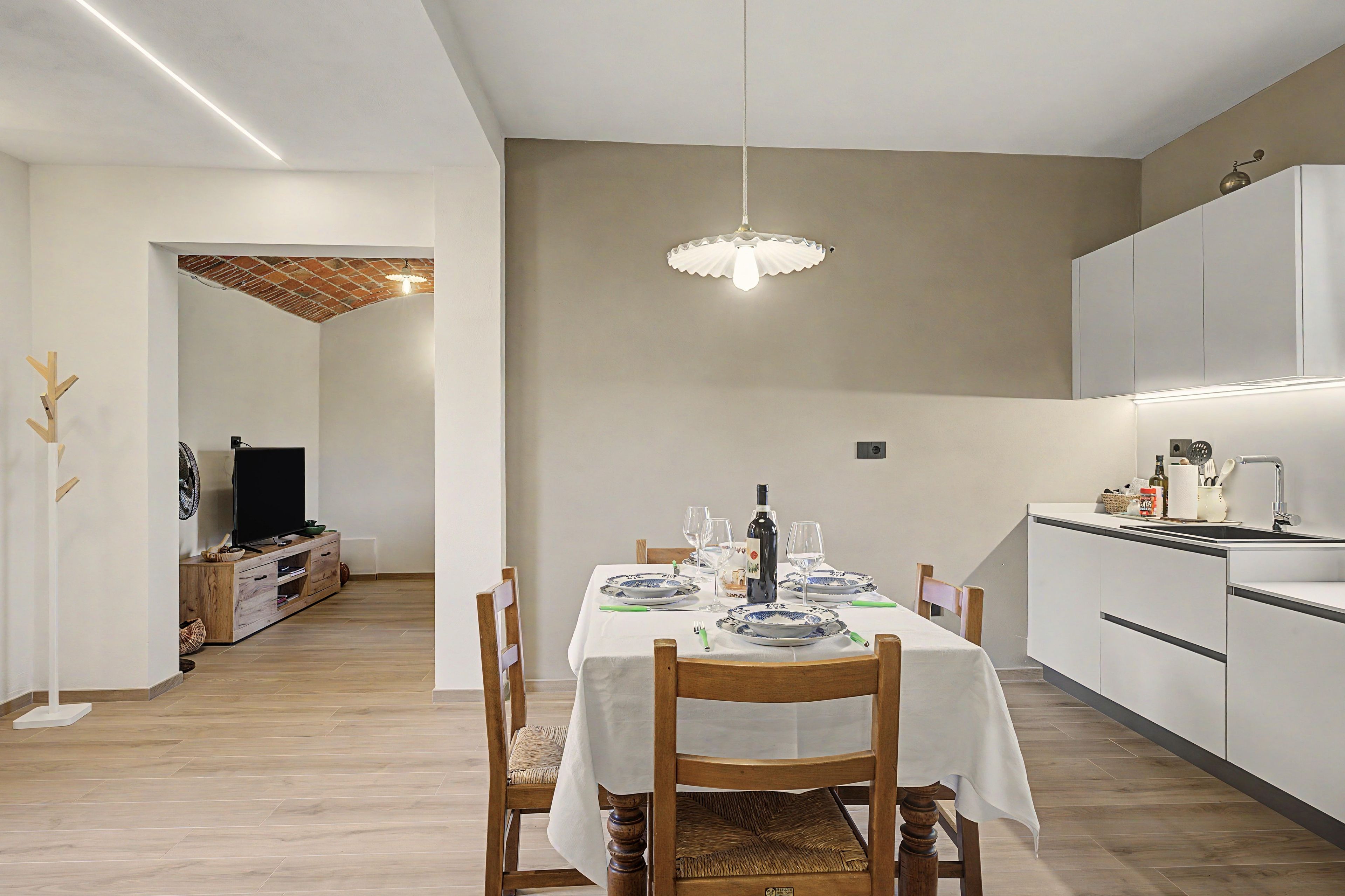 Un comedor moderno con una mesa dispuesta para dos, una lámpara colgante y una cocina al fondo.