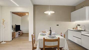 Un comedor moderno con una mesa dispuesta para dos, una lámpara colgante y una cocina al fondo.