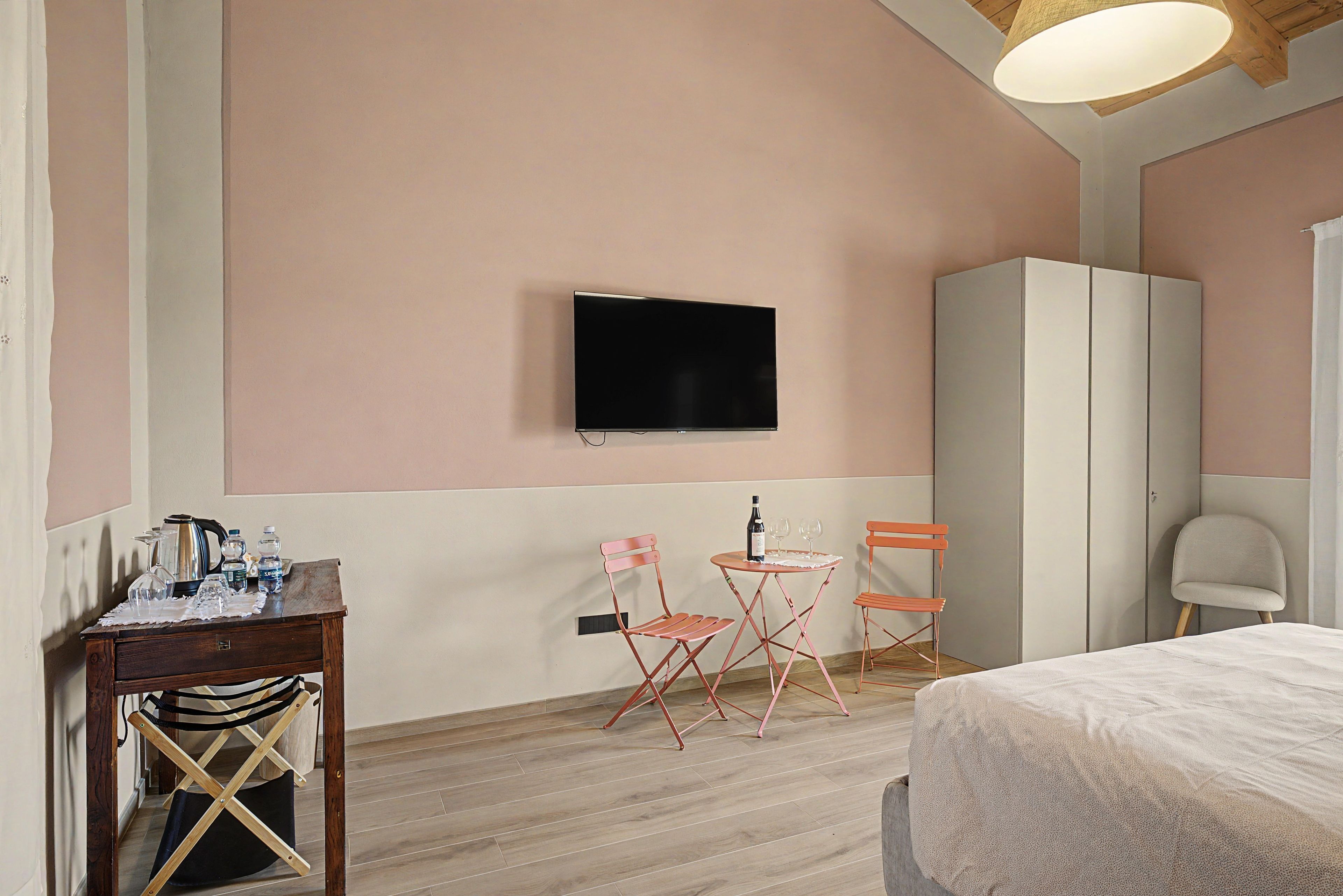 A bedroom with a bed, a television mounted on the wall, a wardrobe, and a small table with a chair.