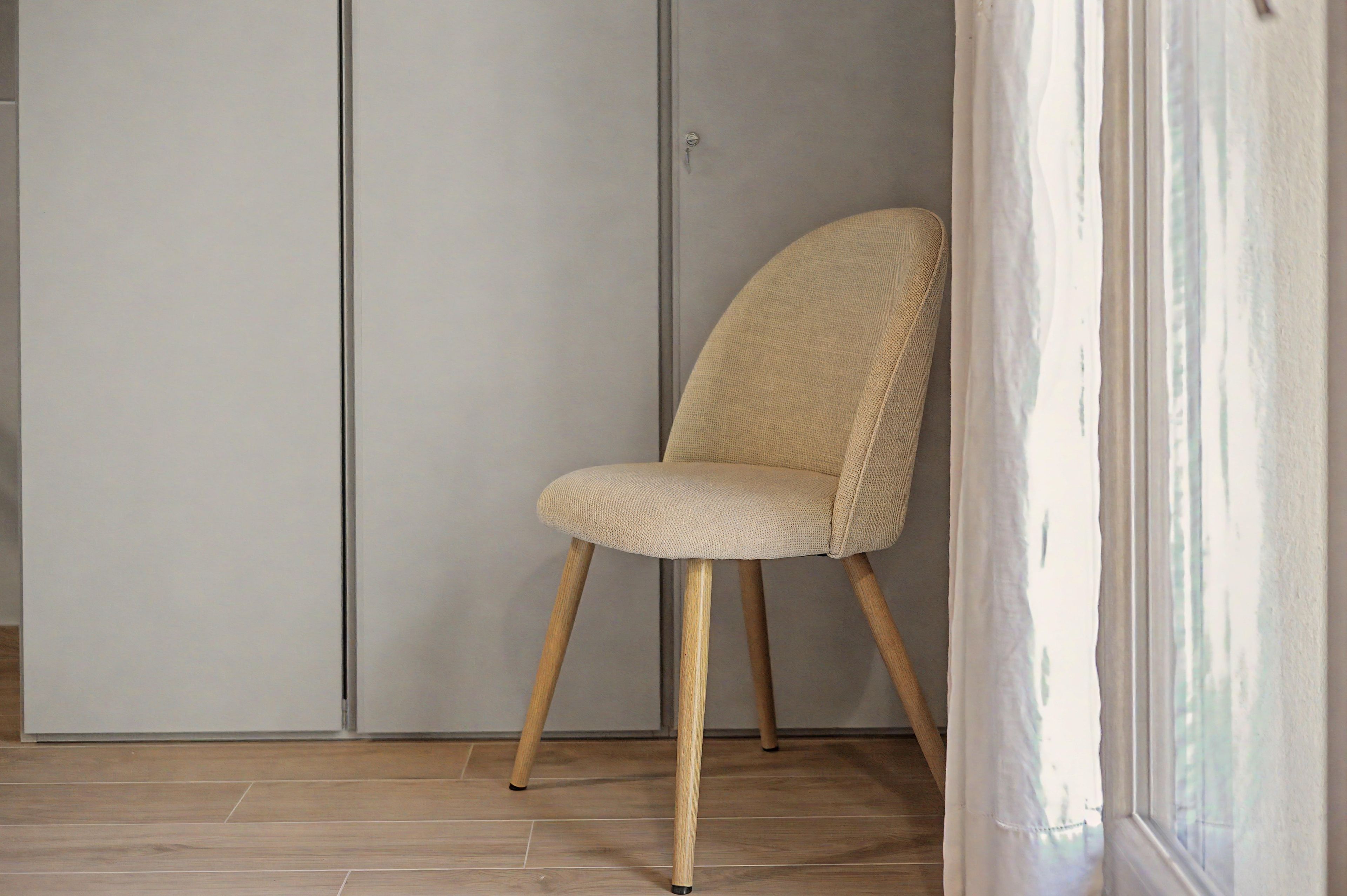 Una sedia con seduta e schienale intrecciati, gambe di legno e un muro grigio sullo sfondo.