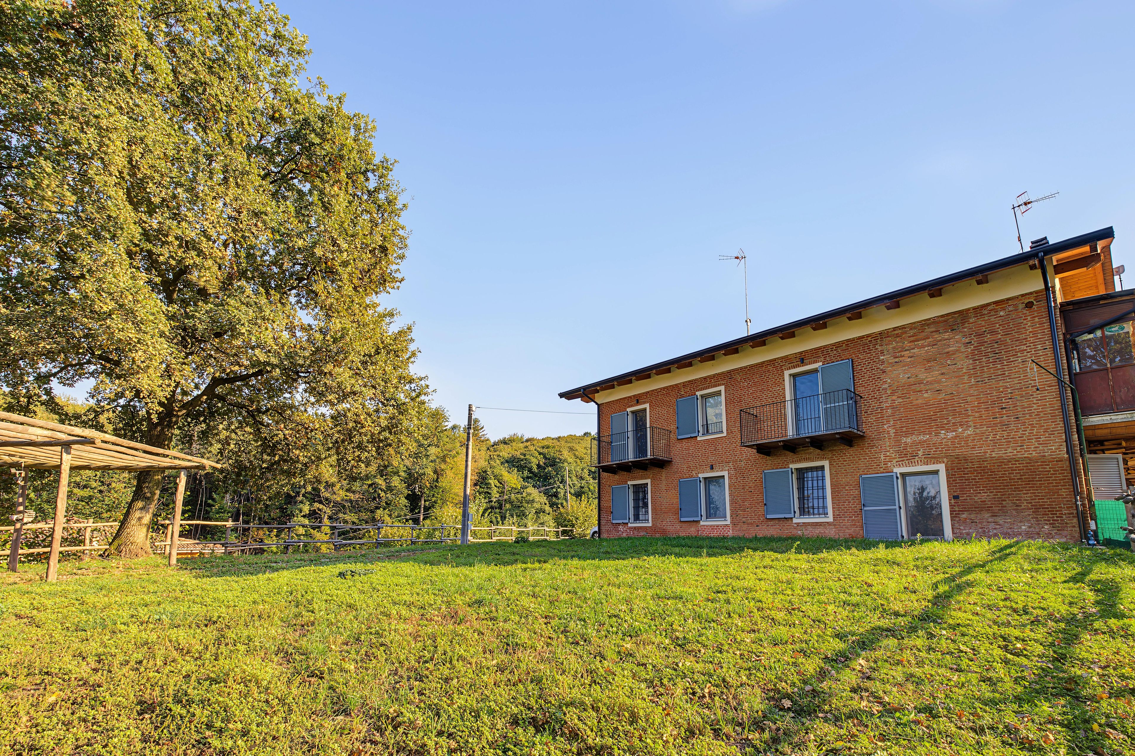 Un edificio in mattoni di due piani con tetto piatto, una pergola in legno e un prato in primo piano.