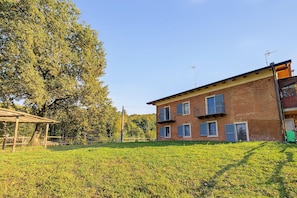 Un edificio in mattoni di due piani con tetto piatto, una pergola in legno e un prato in primo piano.