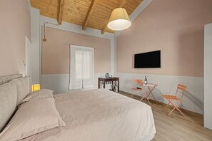 Una camera da letto con un letto, una TV fissata al muro, un tavolino con una sedia e un soffitto in legno.