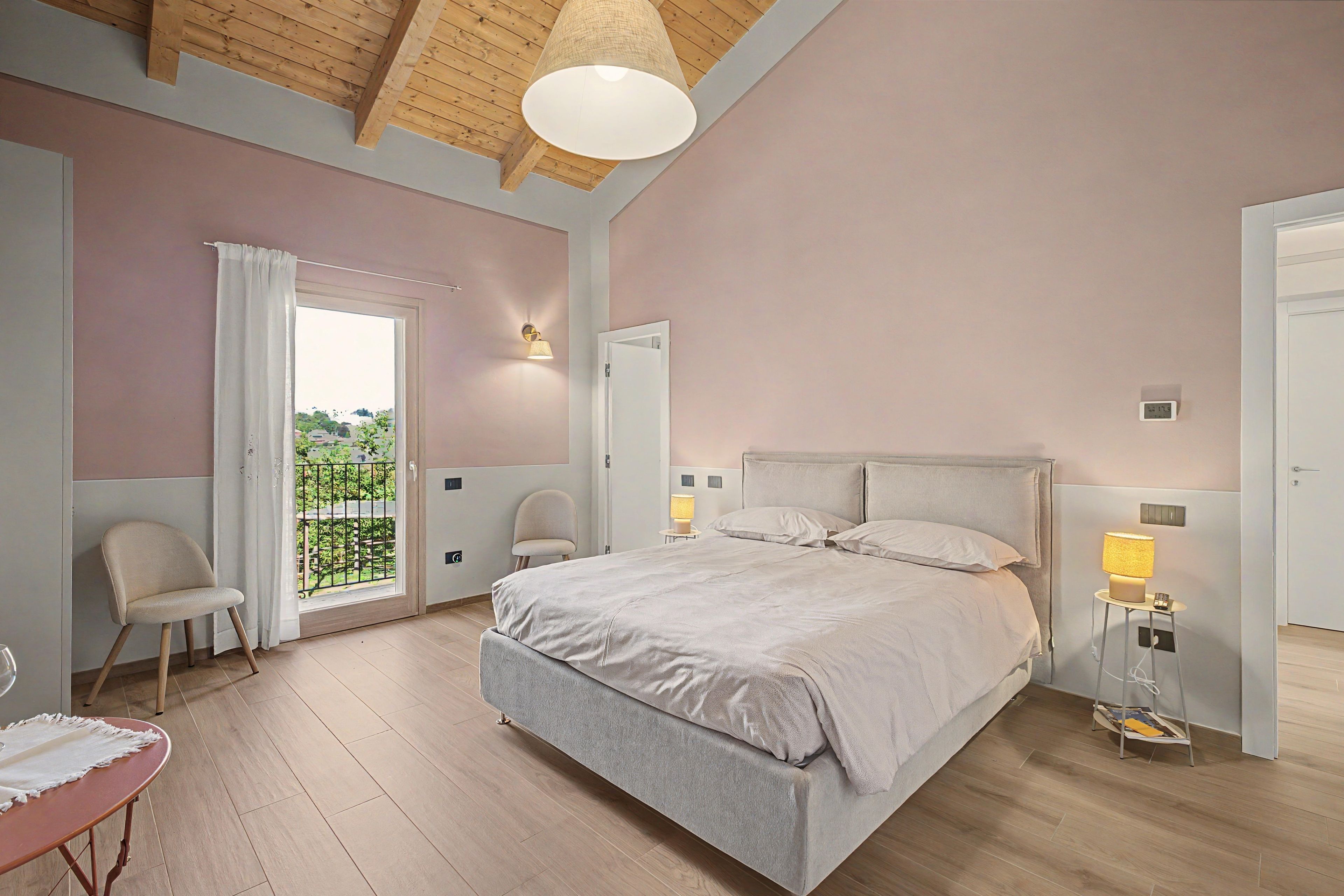 A bedroom with a bed, two chairs, a table, a window with a view, and a ceiling light fixture.