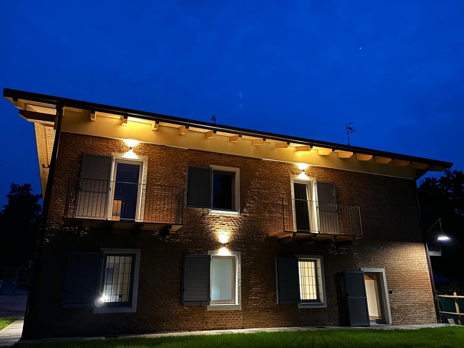 Une maison à deux étages, construite en briques, avec de nombreuses fenêtres, dont certaines sont dotées de volets, et un balcon.