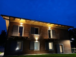 Una casa a due piani in mattoni con diverse finestre, alcune dotate di persiane, e un balcone.