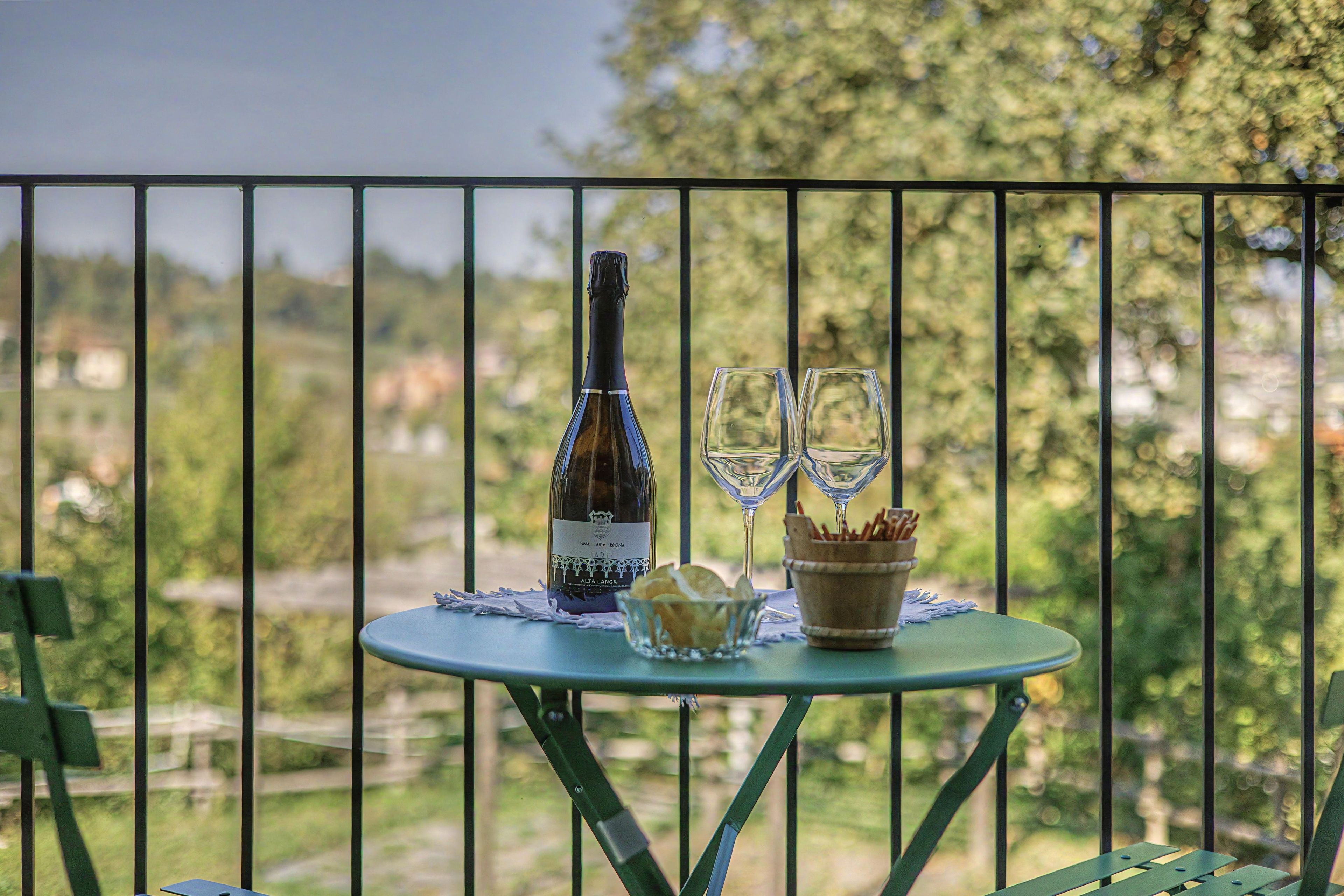 A table with a bottle and two glasses on a balcony overlooking a landscape.