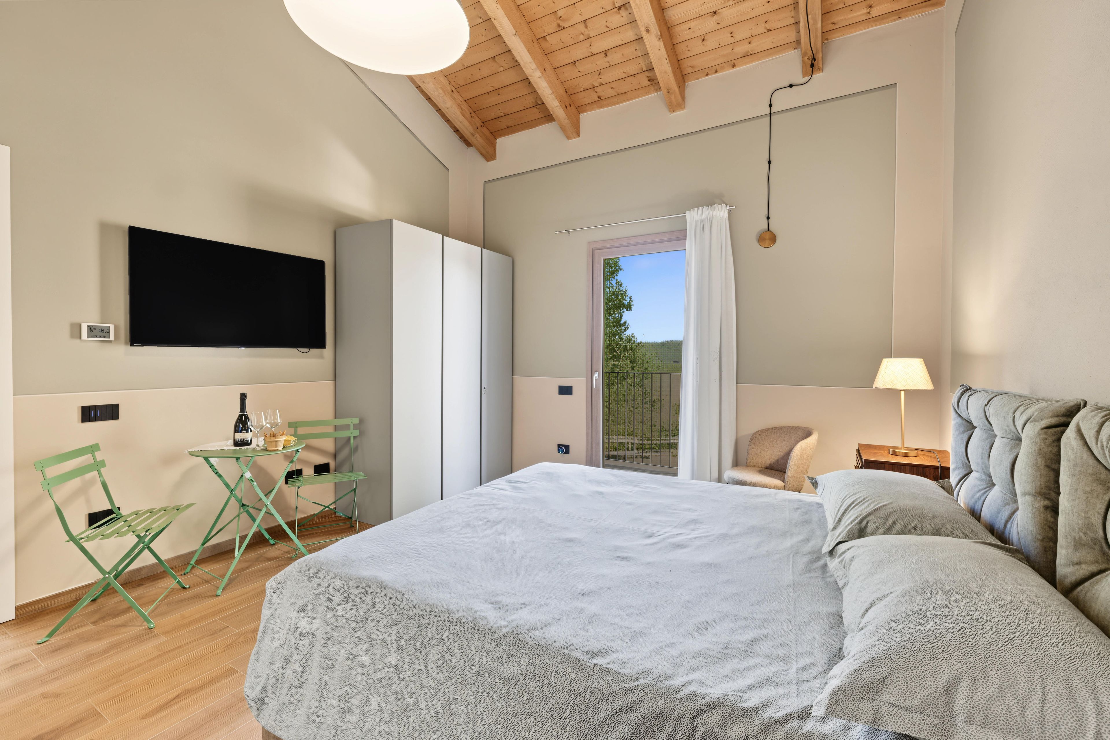 Une chambre à coucher avec un lit, une télévision, une table avec une bouteille et des verres, et une chaise.