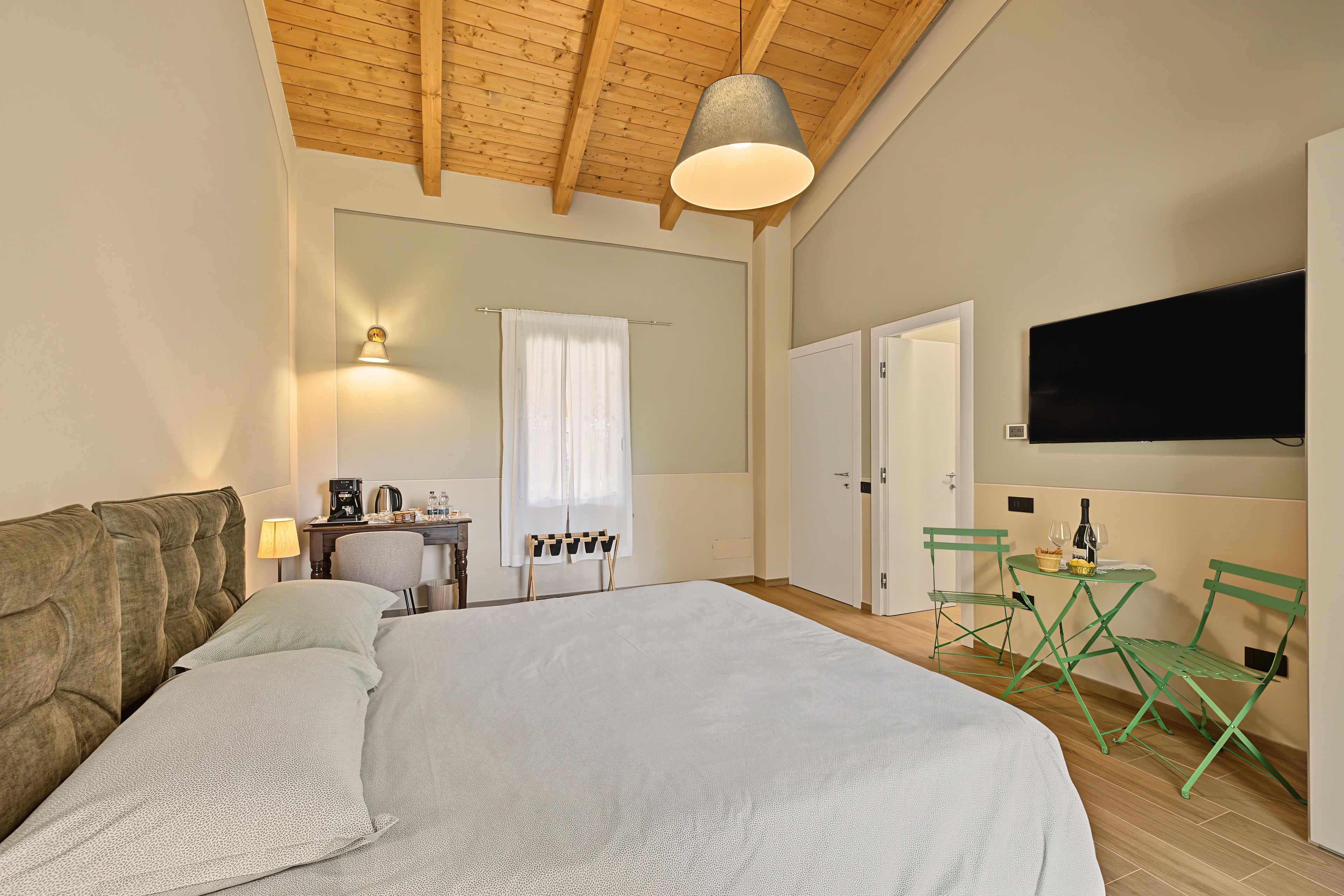 Una camera d'albergo con un letto, una scrivania con una macchina del caffè, una televisione e un angolo salotto con poltrone.