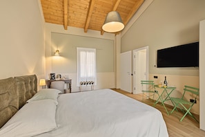 Una camera d'albergo con un letto, una scrivania con una macchina del caffè, una televisione e un angolo salotto con poltrone.