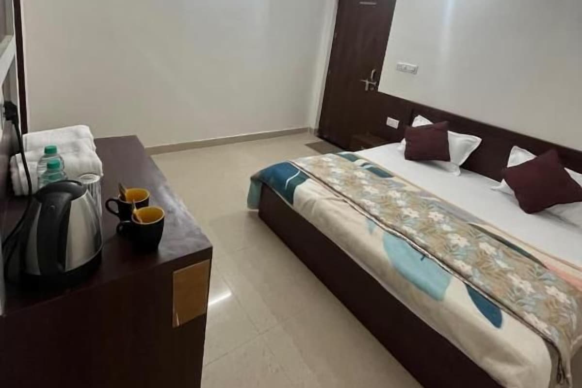 A hotel room with a bed, a desk with a kettle and cups, a ceiling fan, and a door.