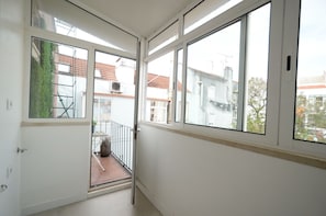 A corridor with large windows, a door, and a view of a residential area with buildings and a balcony. - New Listing (Lisboa)