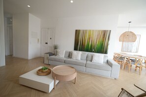 A modern living room with a grey sofa, round coffee table, and a dining area with wooden furniture. - New Listing (Lisboa)