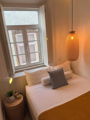 Une chambre à coucher avec un lit, des oreillers, une lampe de chevet, un luminaire suspendu et une fenêtre donnant sur un paysage.