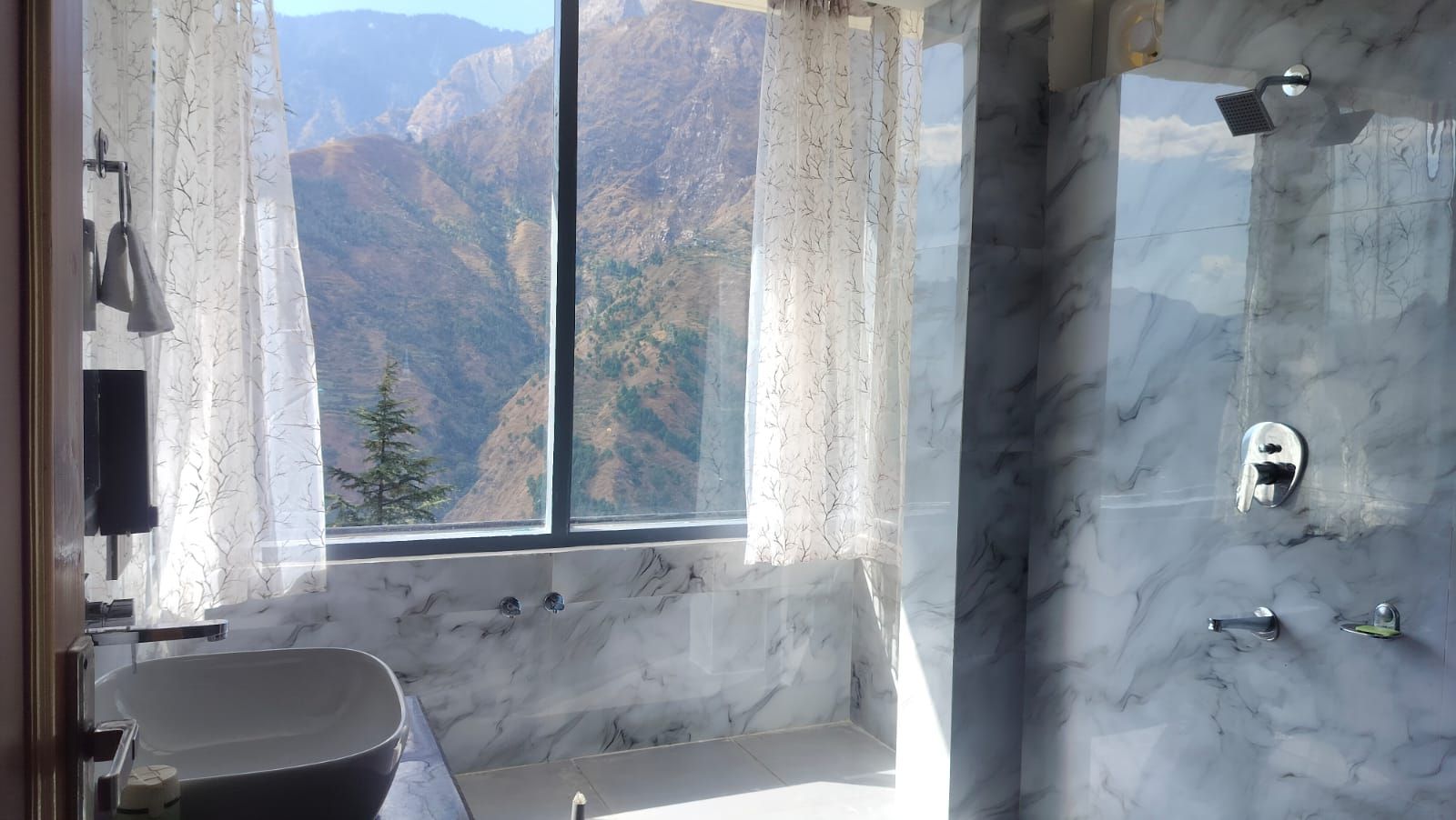 A bathroom with a bathtub, a shower, and a window with a mountain view.