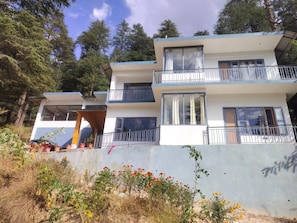 Un edificio de varios pisos con balcones, grandes ventanales y un paisaje natural circundante.