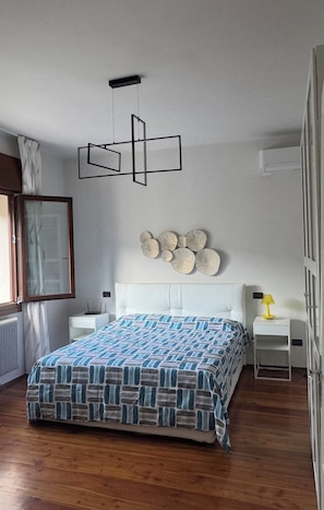 A bedroom with a bed, bedside tables, a wall-mounted light fixture, and a window with curtains. - New Listing (Vittorio Veneto)