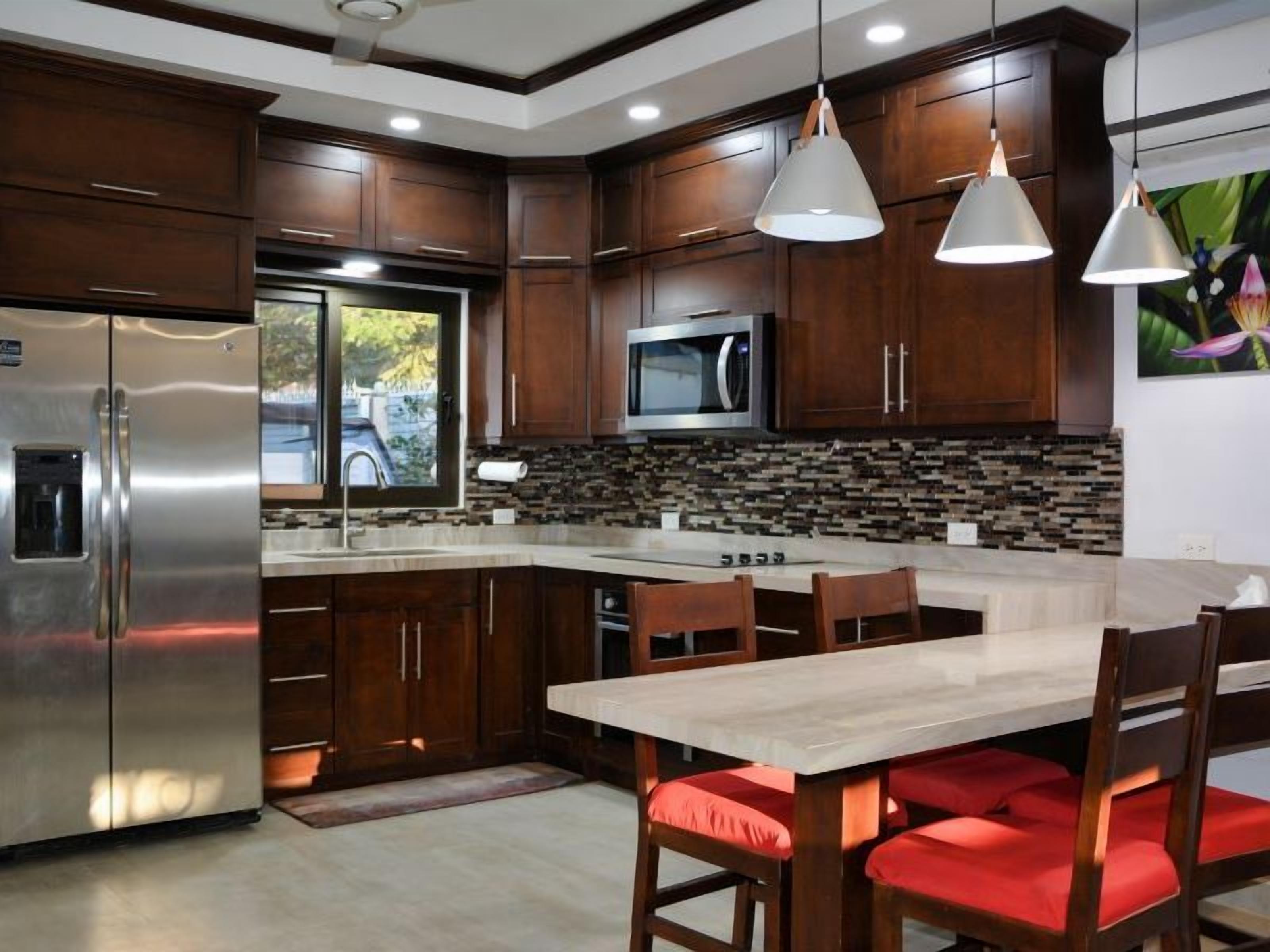 A modern kitchen with dark wood cabinets, stainless steel appliances, and a central island with red cushioned chairs.