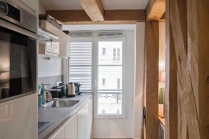 A compact kitchen with a built-in oven, a sink, and a window with blinds. -  Studio Apartment Overlooking Luxembourg Gardens - Latin Quarter (Paris)