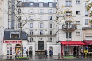 Um edifício de vários andares com arquitetura europeia tradicional, destacando uma entrada central com portão preto e lojas no andar térreo.