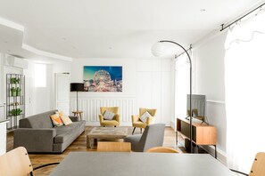 Uma sala de estar moderna com um sofá, poltronas, uma mesa de centro, um rack para TV e uma grande pintura de uma roda gigante.