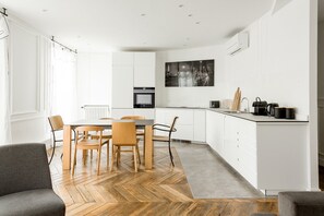 Cozinha moderna com armários brancos, uma mesa de jantar com cadeiras e piso com padrão herringbone.