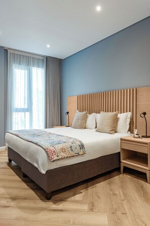 Moderni hotellihuone, jossa on suuri sänky, puinen pääty ja yöpöytä, jossa on lamppu.