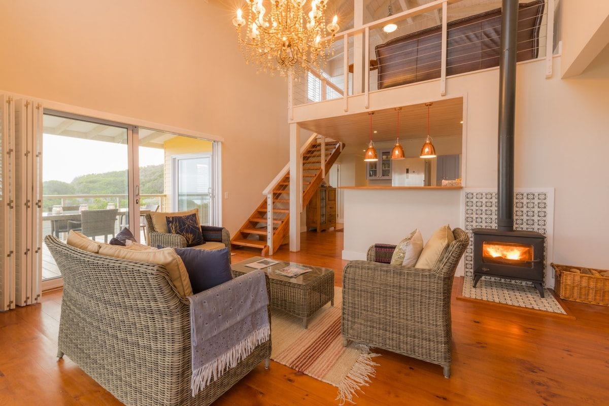 A spacious living room with wicker furniture, a fireplace, and a staircase leading to an upper level.